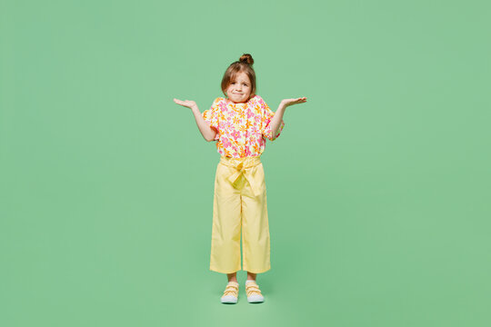 Full Body Sad Little Child Kid Girl 6-7 Years Old Wear Casual Clothes Shrugging Shoulders Looking Puzzled Isolated On Plain Pastel Green Background Studio. Mother's Day Love Family Lifestyle Concept.