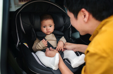 happy father is fastening safety belt to infant baby in car seat