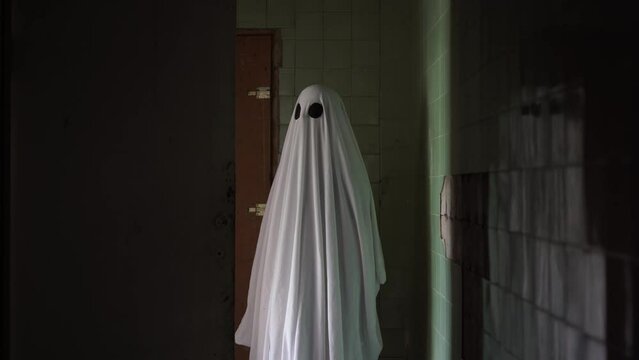 A ghost in a white sheet walks in an old abandoned house, happy Halloween