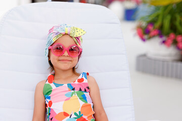 Funny cute baby girl on summer vacation. Child having fun in swimming pool. Sweet toddler girl in colorful swimsuit and sunglasses relaxing on sunbed.