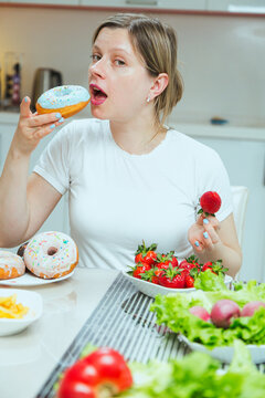 Woman holding donuts and strawberries on plates in hands, the concept of picking healthy snacks against unhealthy ones. Nature sugar or sugar from donuts