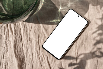 Empty smartphone screen mockup on beige linen tablecloth with aesthetic sun light shadow, lifestyle...