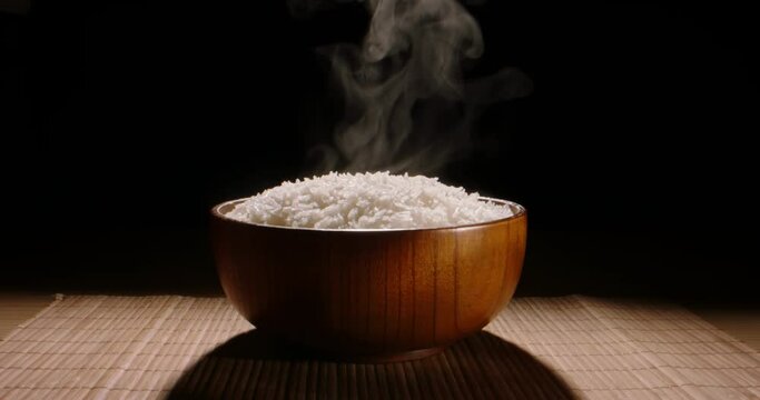 Hot white cooked rice steam bowl black background slow motion, Close up. Sticky rice after cooked. Asian Chinese Thai Japanese Indian traditional meal. Vegetarian boiled organic healthy nutrition