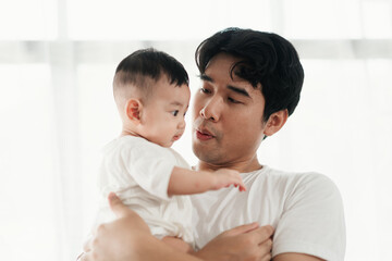 Happiness of fatherhood. Young Asian dad with adorable baby on his hands standing near window at home. Loving father spending time with infant child. Fathers day concept.