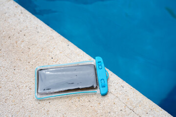 Waterproof case with a smartphone on the background of the pool on a sunny summer day.