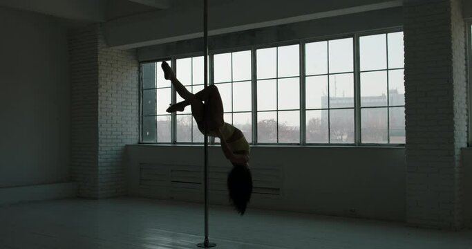 Asian strip pole dancer Silhouette twirling on pole bright studio big windows background. Slow motion. In light underwear, freedom, woman power, brunette. Beautiful figure, body, chest, buttocks