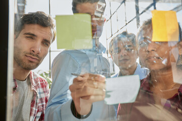 A group of business people behind a glass wall in the office sticking notes