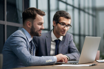 Fototapeta premium Two young businessmen sitting at workplace and working together in office