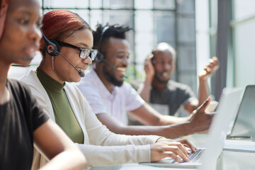 Fototapeta premium Smiling beautiful African American woman working in call center with diverse team
