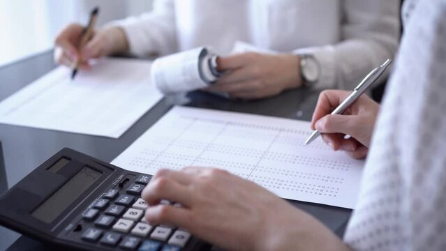Two accountants use a calculator and laptop computer for counting taxes or revenue balance while rolls of receipts are waiting to be calculated. Business audit, and taxes concepts