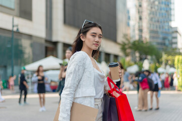 A pretty asian female office employee taking a walk to work at the city business district. Holding a cup of coffee and some shopping bags.