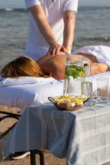 Woman having relax in tropical massage spa on the beach near the sea on massage table. Professional masseur provides back and neck spa procedures.