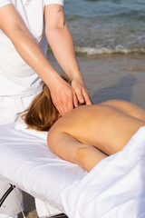 Fototapeta na wymiar Woman having relax in tropical massage spa on the beach near the sea on massage table. Professional masseur provides back and neck spa procedures.