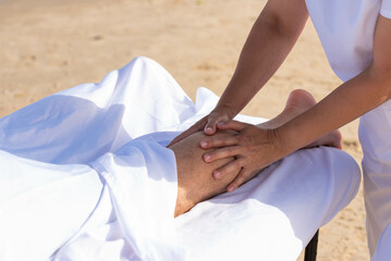 Woman having relax in tropical massage spa on the beach near the sea on massage table. Professional masseur provides leg and foot spa procedures.