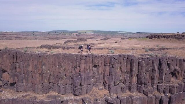 Two photographers carry camera gear along top of basalt column cliff