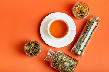 Cup of aromatic green tea and glass jars with leaves of tea from above on orange background. Tasty...