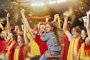 Happy young woman with little girl attending football match, fans cheering up favourite soccer...