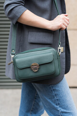 A woman holds a green handbag in the city. Close-up image. The concept of luxury