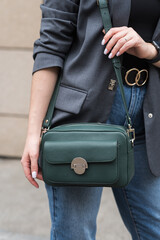 A woman holds a green handbag in the city. Close-up image. The concept of luxury