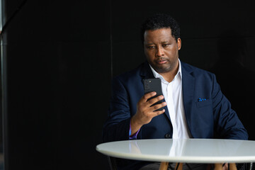 Portrait of handsome black man wearing suit and using mobile phone while sitting