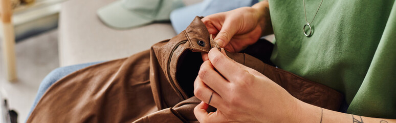 cropped view of young and tattooed woman checking button on leather pants during clothes...