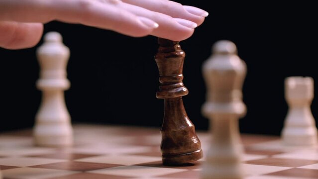 Caucasian Woman's Hand Knocks Over King Chess Piece on Rotating Chess Board, Close-up Macro. Shot with ARRI Alexa in ArriRaw at 120 fps, exported 23.98 fps QuickTime Apple ProRes 422 HQ.