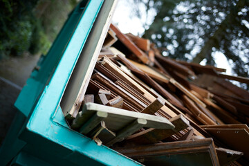 green recycling container filled with wood, next to a house