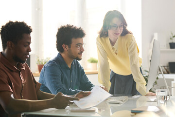 Business colleagues looking at monitor and discussing online presentation in team in office