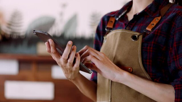 Close-up hand of beautiful asian woman standing holding tablet in hand. Used to check the inventory of the bakery, the number of cakes and desserts left for sale. A woman owns a bakery in overalls.