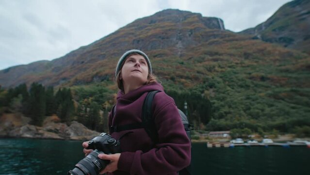 Young woman photographer look around epic norwegian landscape and make photos of mountains and fjord. Inspiring travel wanderlust adventure around europe