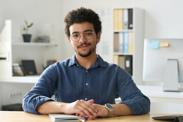 Portrait of young businessman in eyeglasses looking at camera while sitting at his workplace in...