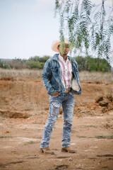 Naklejka na ściany i meble Cowboy wearing jeans and a hat, standing under the sky with fluffy clouds, working on a farm
