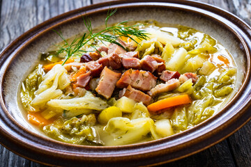 Bowl of hot cabbage soup with bacon on wooden table
