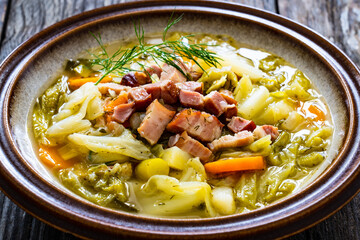 Bowl of hot cabbage soup with bacon on wooden table
