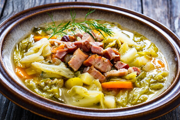 Bowl of hot cabbage soup with bacon on wooden table
