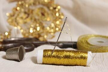 Spool of Gold Thread and Scissors With Thimble on Off White Fabric With Gold Sequins