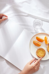 A dish in round-shaped with orange slices and egg tarts placed on, decorated with a glass of water. Mockup on blank paper