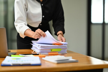 Cropped image of female bookkeeper checking unfinished accountancy report on wooden office desk