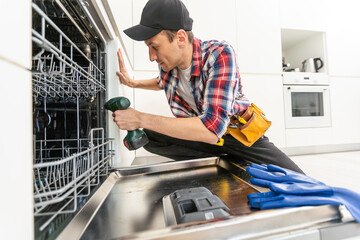 Worker using screwdriver to repair dishwasher at home stock photo