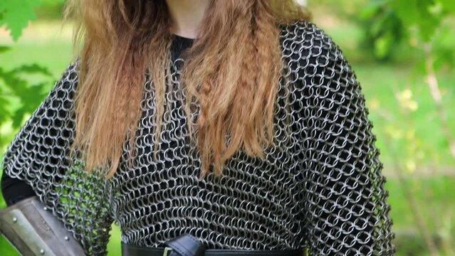 Smooth camera movement, selective focus, portrait of a young woman in chain mail and bracers with a bow in her hands against the backdrop of a summer forest.
