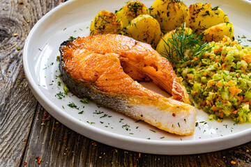 Seared salmon steak with fried potatoes and fresh cabbage  salad served on wooden table
