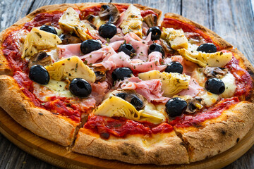 Pizza capricciosa with cooked ham, mozzarella, artichoke and vegetables on wooden table 