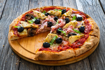 Pizza capricciosa with cooked ham, mozzarella, artichoke and vegetables on wooden table 