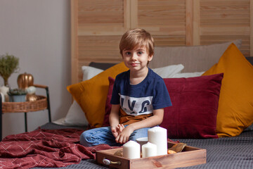 The boy is sitting at home on the bed