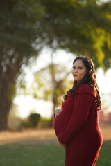 Beautiful happy Asian, Indian pregnant woman holding her belly at home and looking at the camera with a smile.