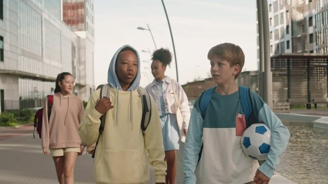 Multiracial preteen boys and girls chatting while walking outdoors together in summer