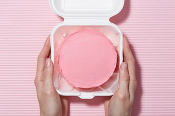Woman holding Korean lunchbox bento cake on pink textured background