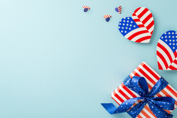 Flag Day festivities. Overhead shot of representative ornaments: hearts with American flag motif and themed giftbox, on a pastel blue background with an empty area for messages or advertising