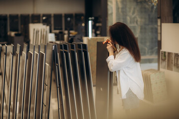 Happy brunette female interior designer choosing flooring tile color texture samples at store shop....