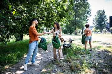 Young volunteers cleaning up park together, collecting trash and holding garbage bags. Responsible...